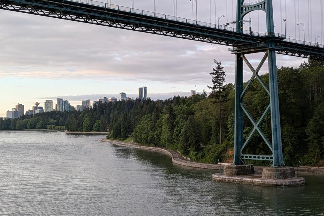 View from a cruise ship balcony sailing directly under the Lions Gate Bridge in Vancouver with the city skyline in the background.
