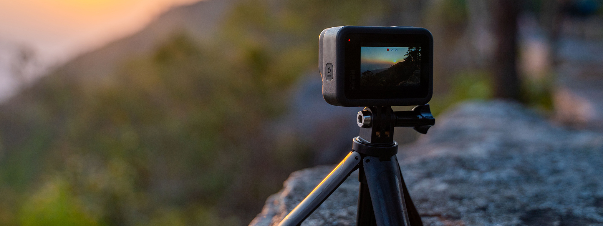 A GoPro mounted on a small tripod outdoors, recording a sunset over the mountains.