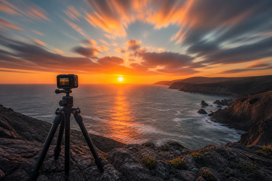 An action camera on a sturdy tripod recording a coastal sunset beneath streaking clouds.
